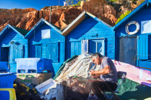 Europa, Portugal, Algarve, Litoral, Barlavento, Distrikt Faro, bei Albufeira, Praia dos Olhos de Agua, Fischer flickt Netze, blaue Fischerhütten vor rotbrauner Steilküste Europa, Portugal, Algarve, Litoral, Barlavento, Distrikt Faro, bei Albufeira, Praia dos Olhos de Agua, Fischer flickt Netze, blaue Fischerhütten vor rotbrauner Steilküste